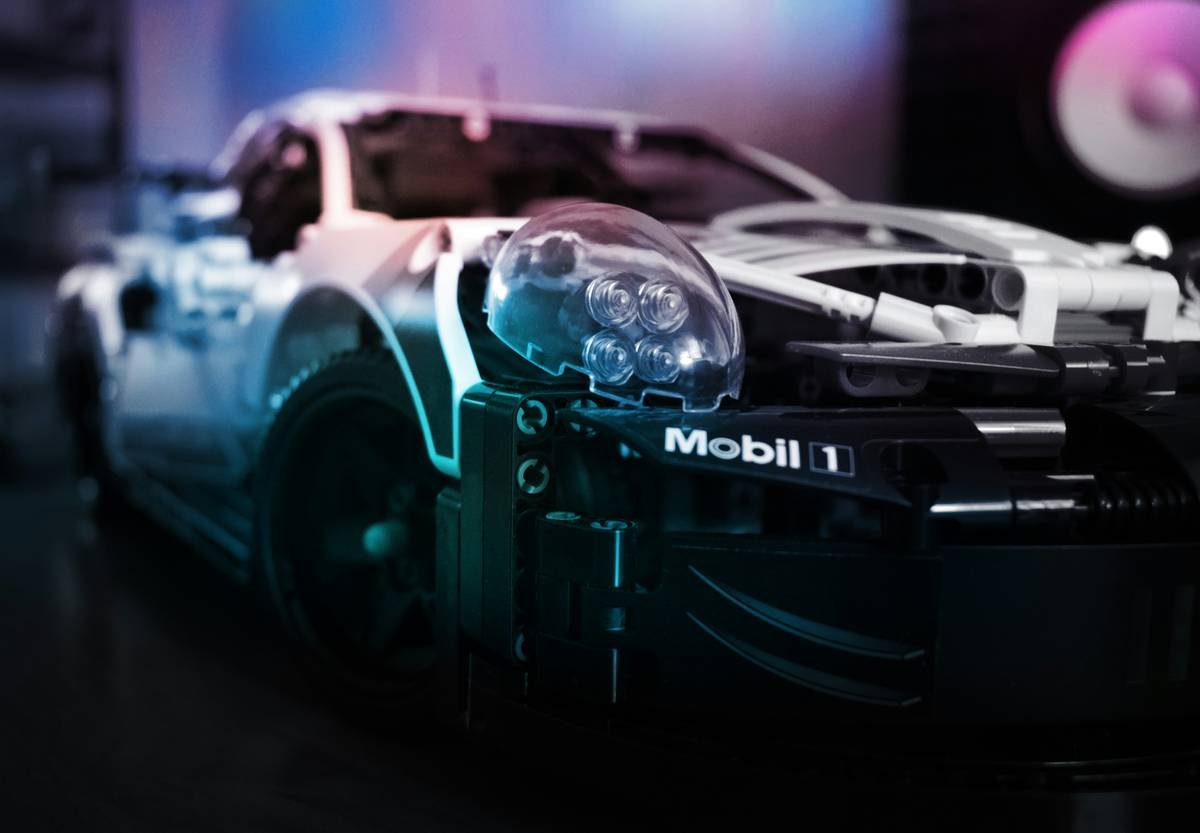 LEGO Porsche with Neon Lighting. A close-up shot of a LEGO Porsche model, illuminated by vibrant neon lights. The neon glow highlights the sleek design and intricate details of the LEGO car, creating a dynamic and futuristic atmosphere