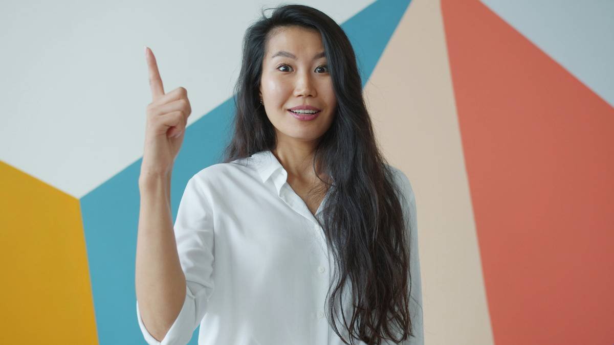 Portrait of creative Asian woman raising finger feeling happy having great idea standing alone on colorful background. Solutions and success concept.